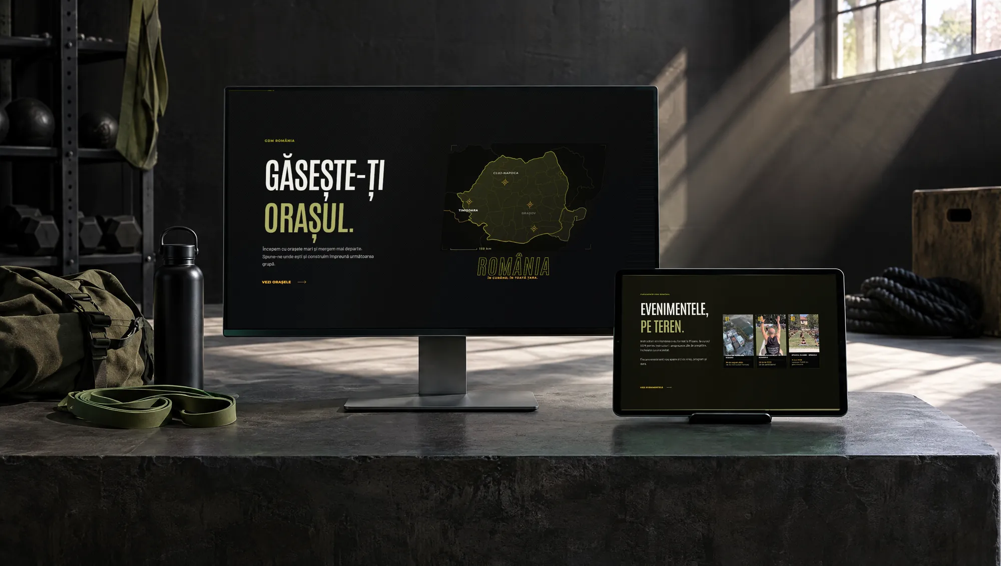 The Gimnastică Dinamică Militară website on a monitor and a tablet in a gym