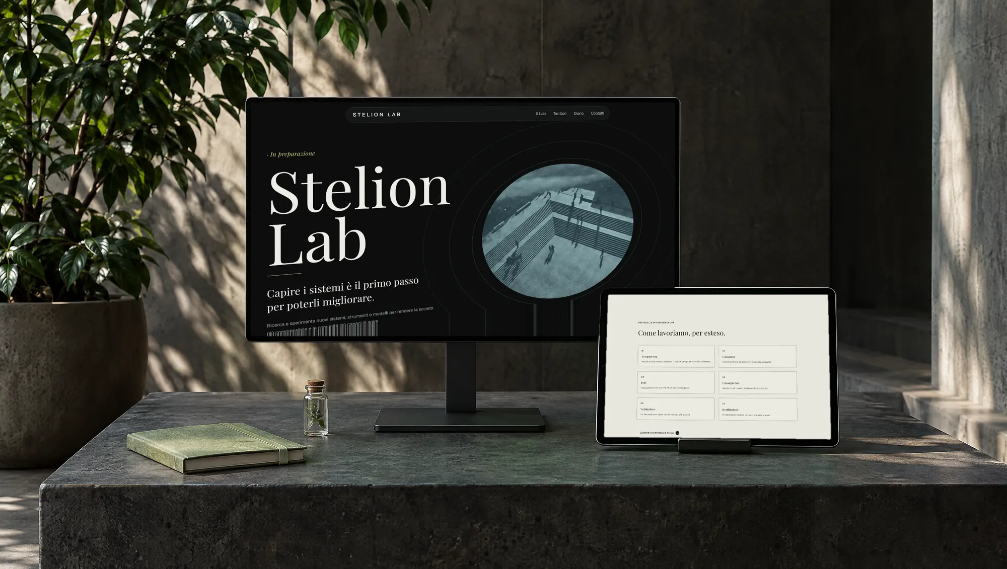 The Stelion Lab website on a monitor and a tablet, on a dark concrete plinth